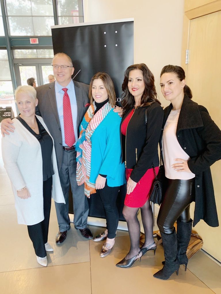 Five people posing indoors at a formal event, dressed in suits and dresses.