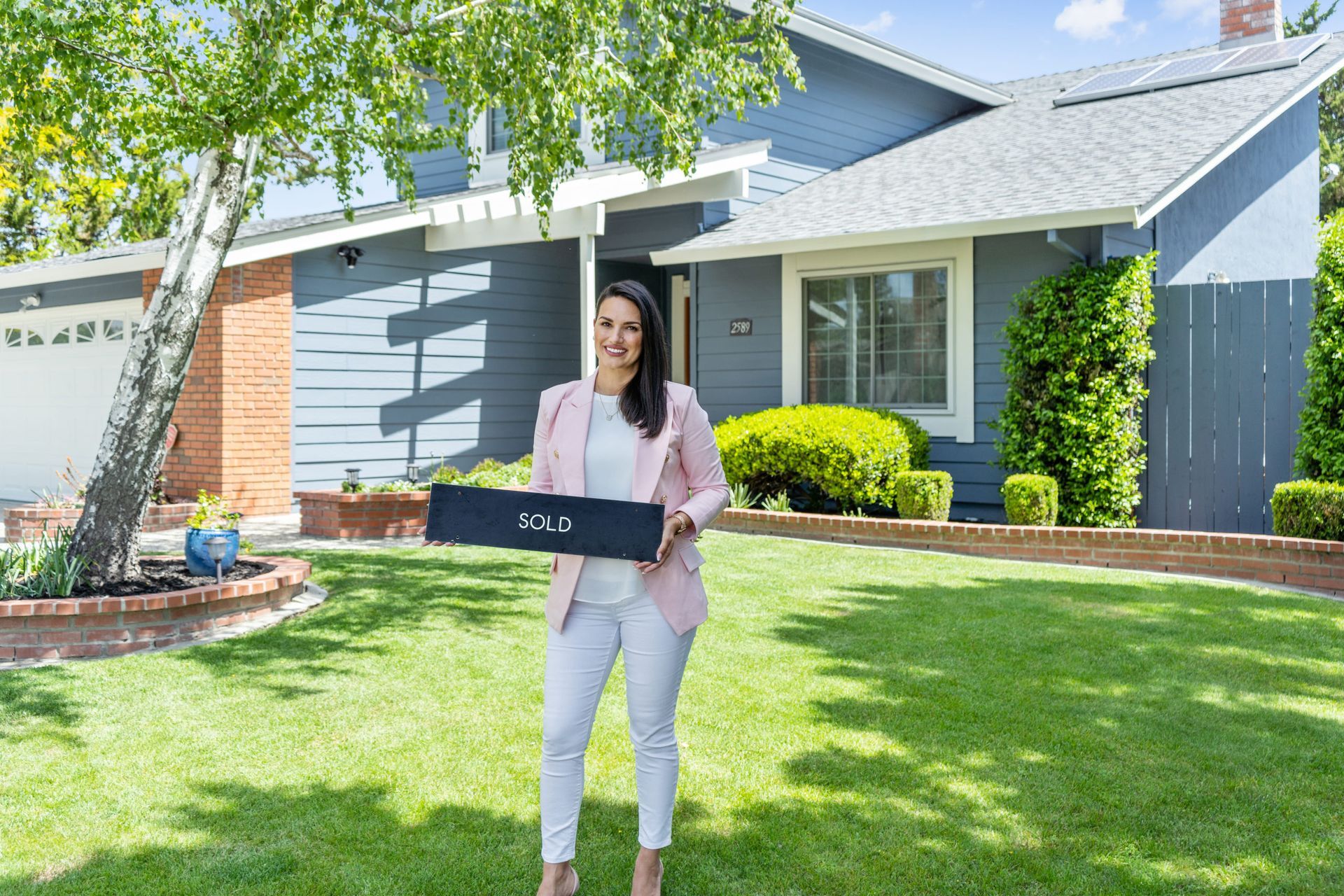 Woman holding a black box in a sunny front yard outside a house