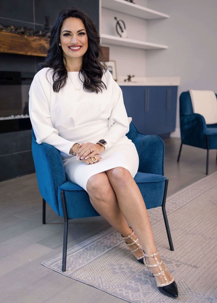 Eva Tia in a white dress is sitting in a blue chair.