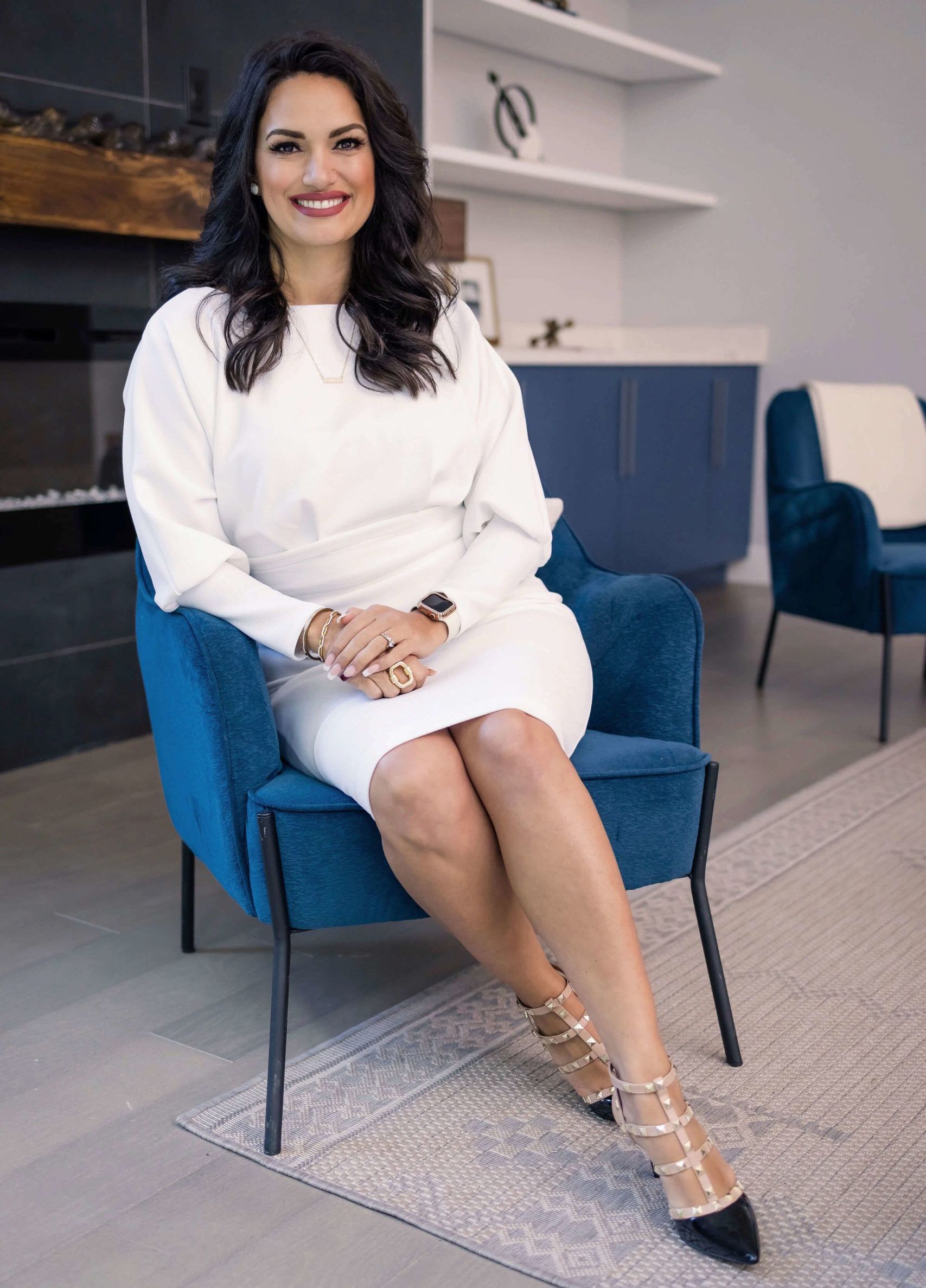 Eva Tia in a white dress is sitting in a blue chair.