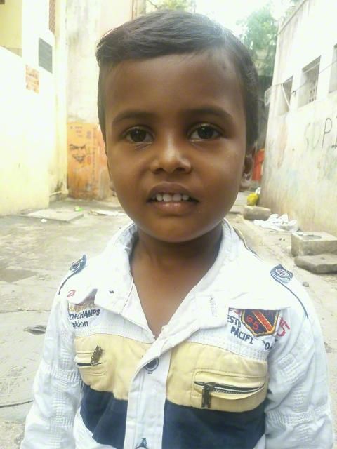 Child standing in a narrow alley, wearing a white shirt and looking at the camera.
