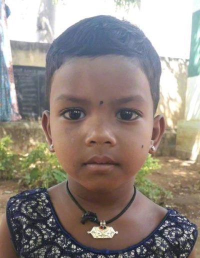 Young child wearing a dark patterned top and necklace, looking at the camera outdoors