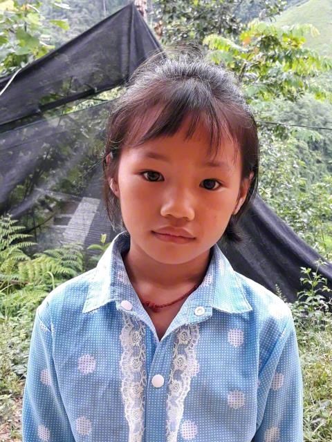 Child standing outdoors in a blue patterned shirt, looking at the camera with a neutral expression.