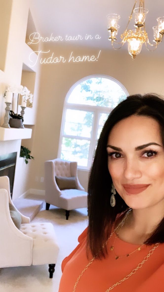 Woman smiling in a bright, elegant living room with white decor and a large arched window.