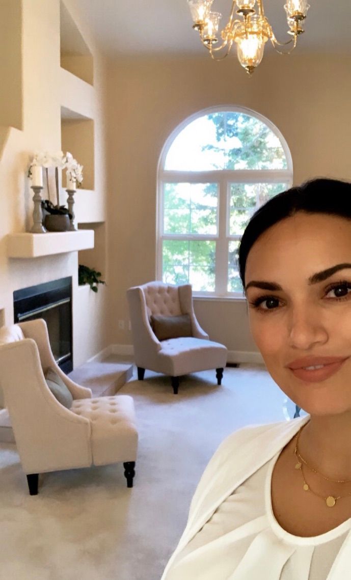 Selfie in a bright living room with fireplace, arched window, chandelier, and cream armchairs