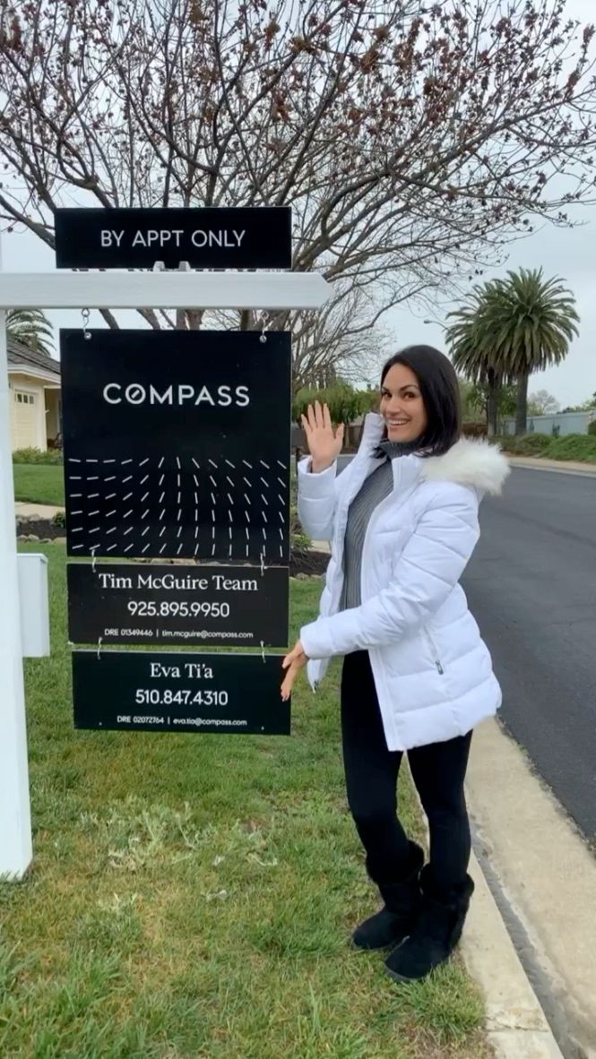 Woman in white coat posing beside a sign for Corn Pass on a sidewalk.