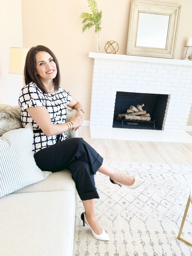 Woman sitting on a white sofa in a bright living room, smiling beside a fireplace and mirror.