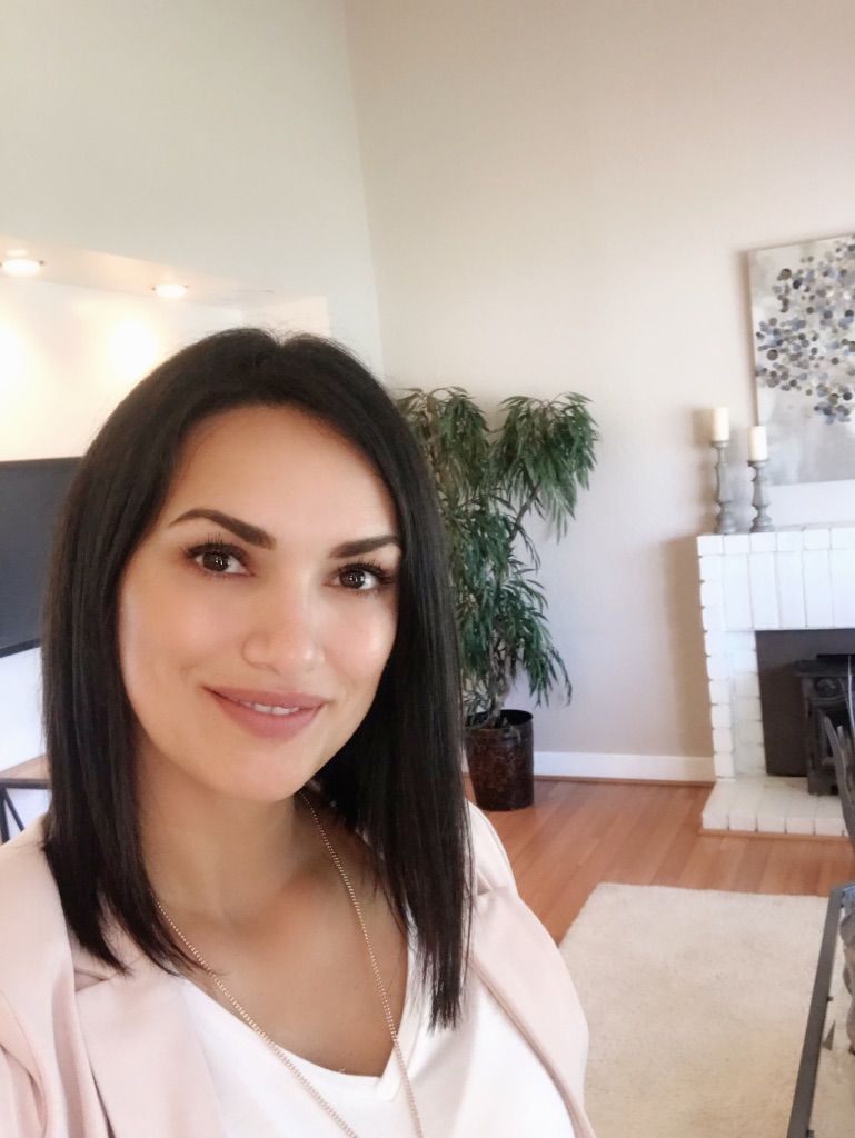 Woman smiling in a bright living room with a fireplace, plant, and hardwood floors.