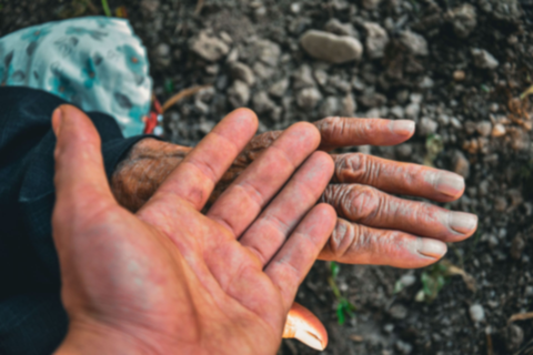 Two dirt-covered hands, one open and one outstretched, over rocky ground.
