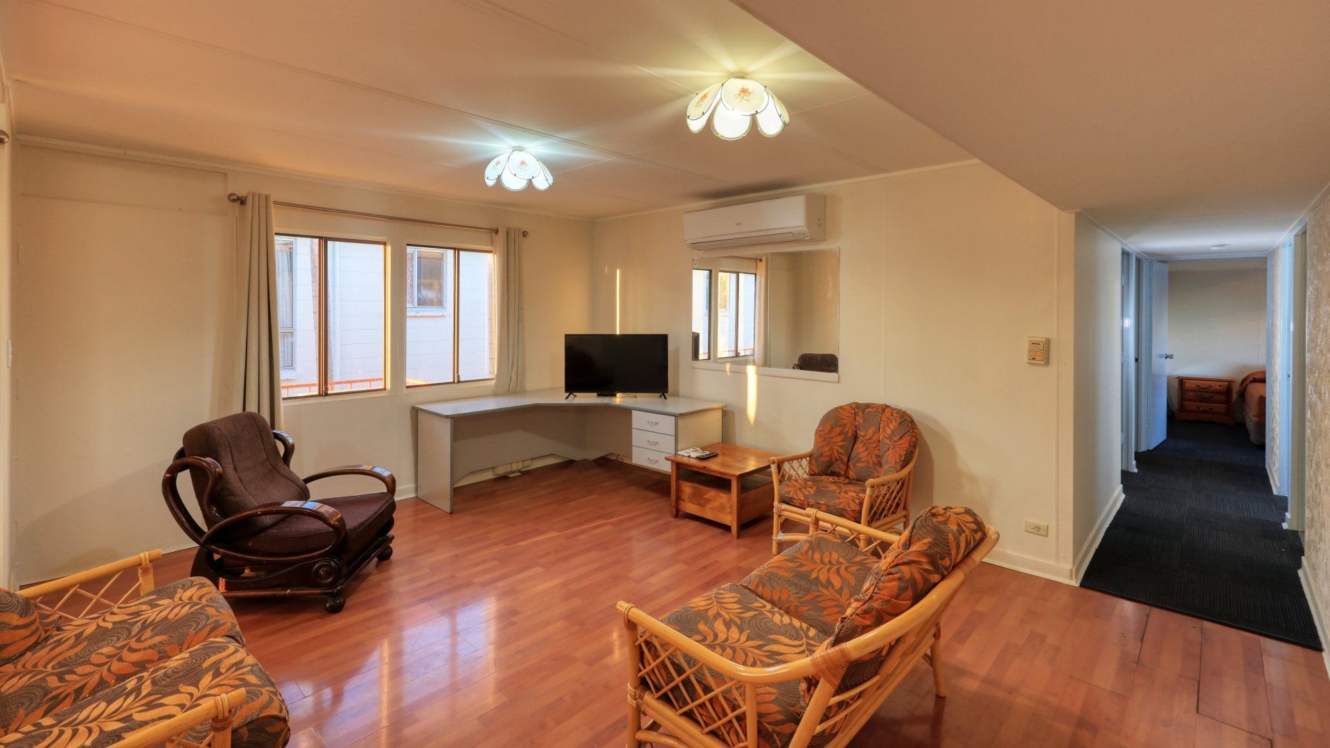 Living Room with Wooden Floors, Rattan Furniture, Tv, Desk, and A Hallway — Townview Motel In Mount Isa, QLD
