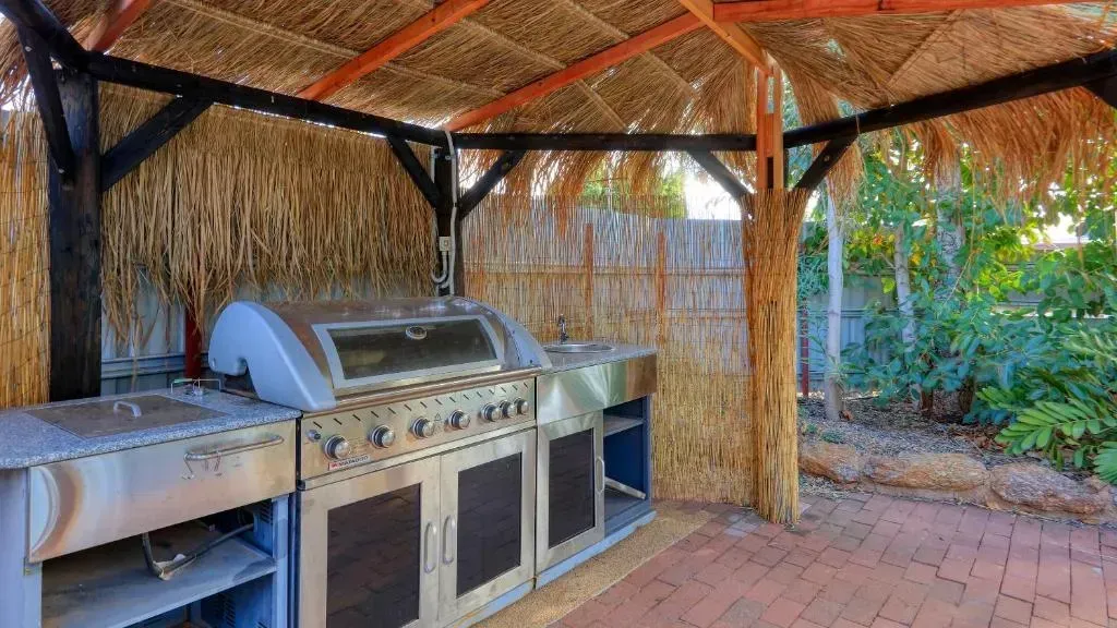 Outdoor Kitchen with Stainless Steel Grill, Cabinets, and Thatched Roof Shelter — Townview Motel In Mount Isa, QLD