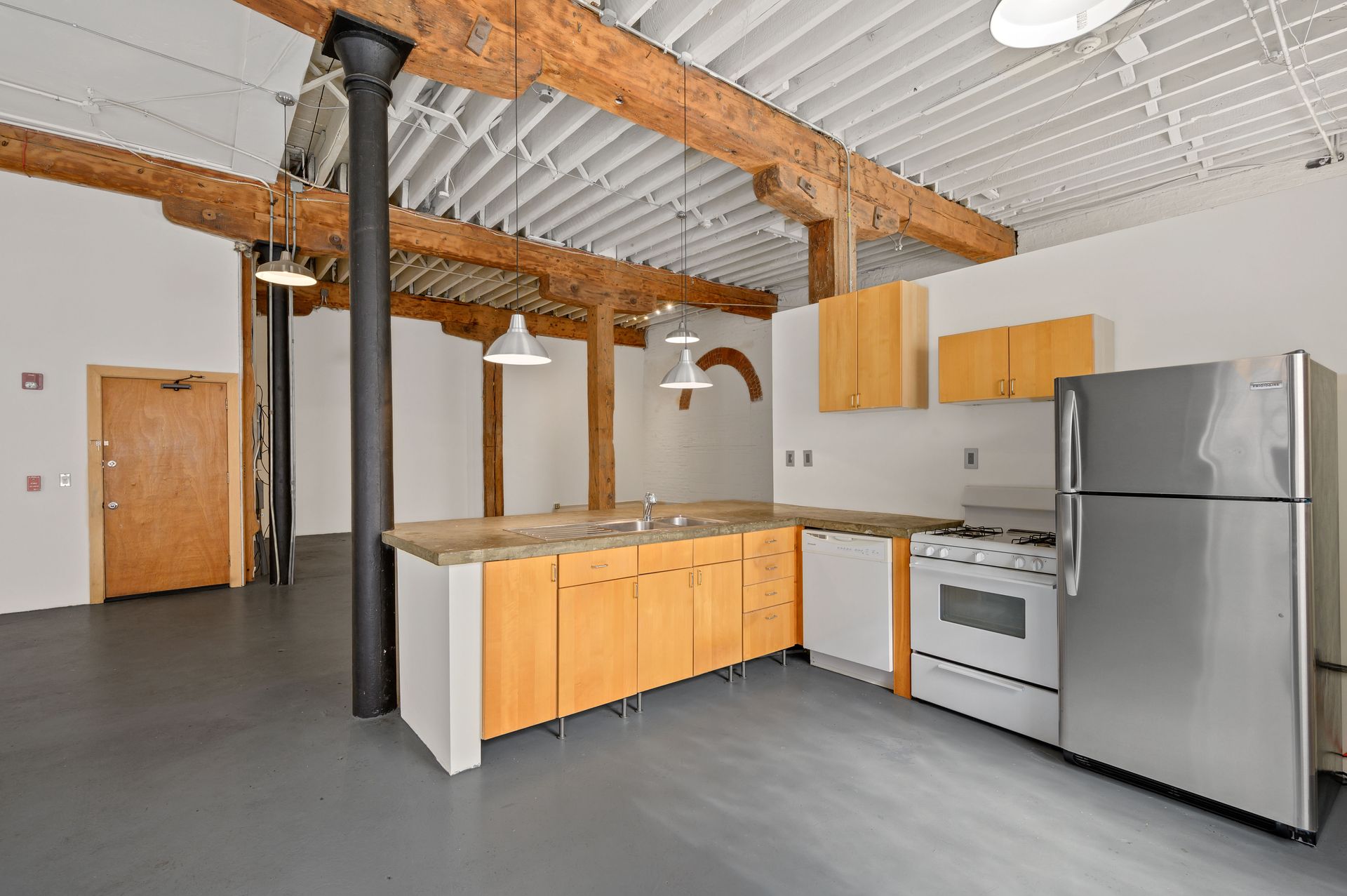 An empty kitchen with stainless steel appliances and wooden cabinets