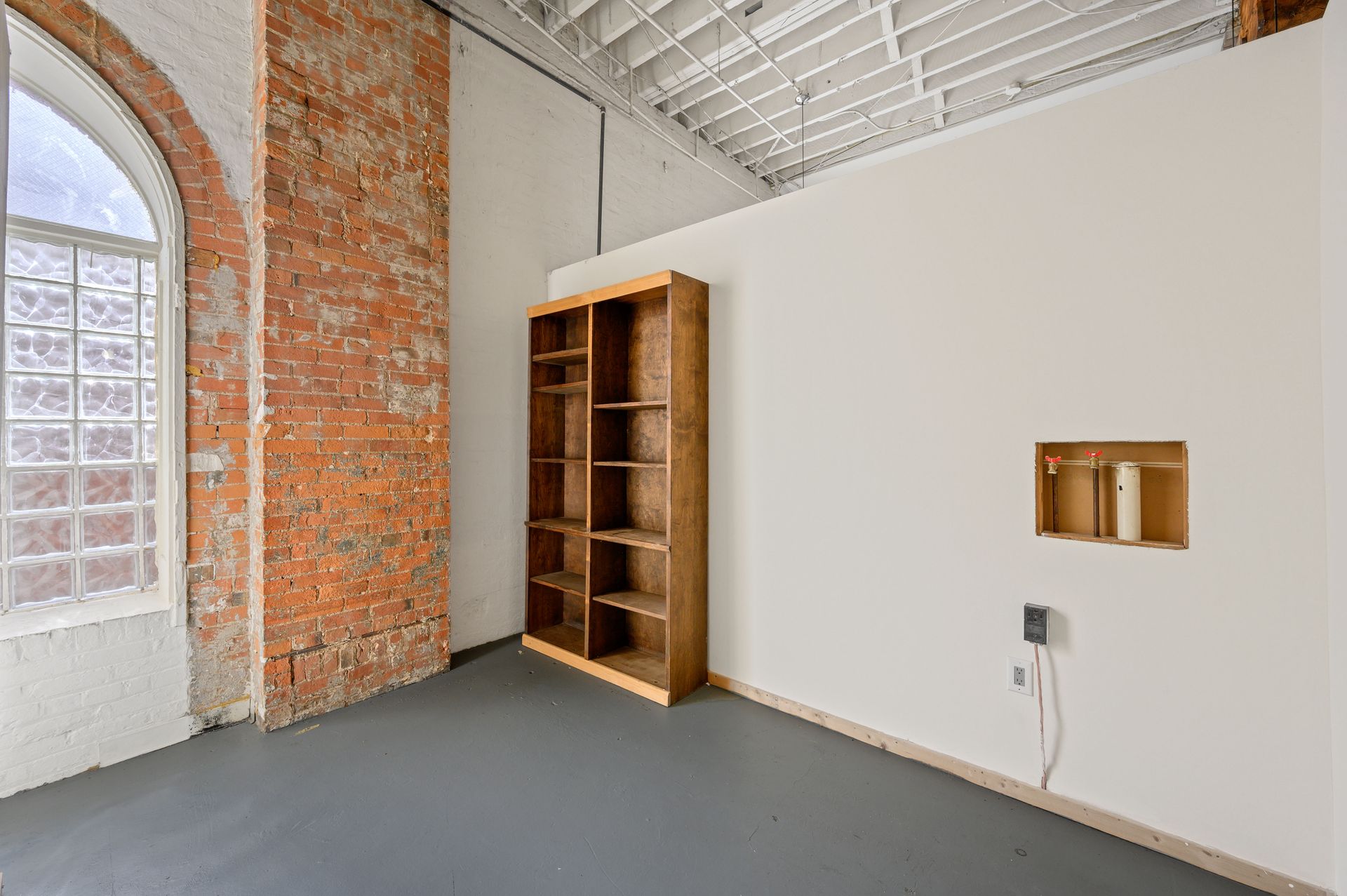 An empty room with a brick wall and a bookshelf.