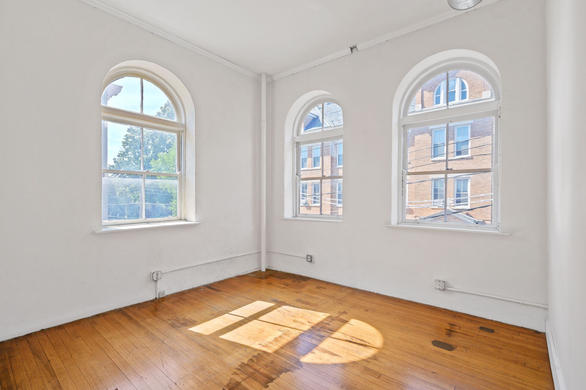An empty room with arched windows and wooden floors.