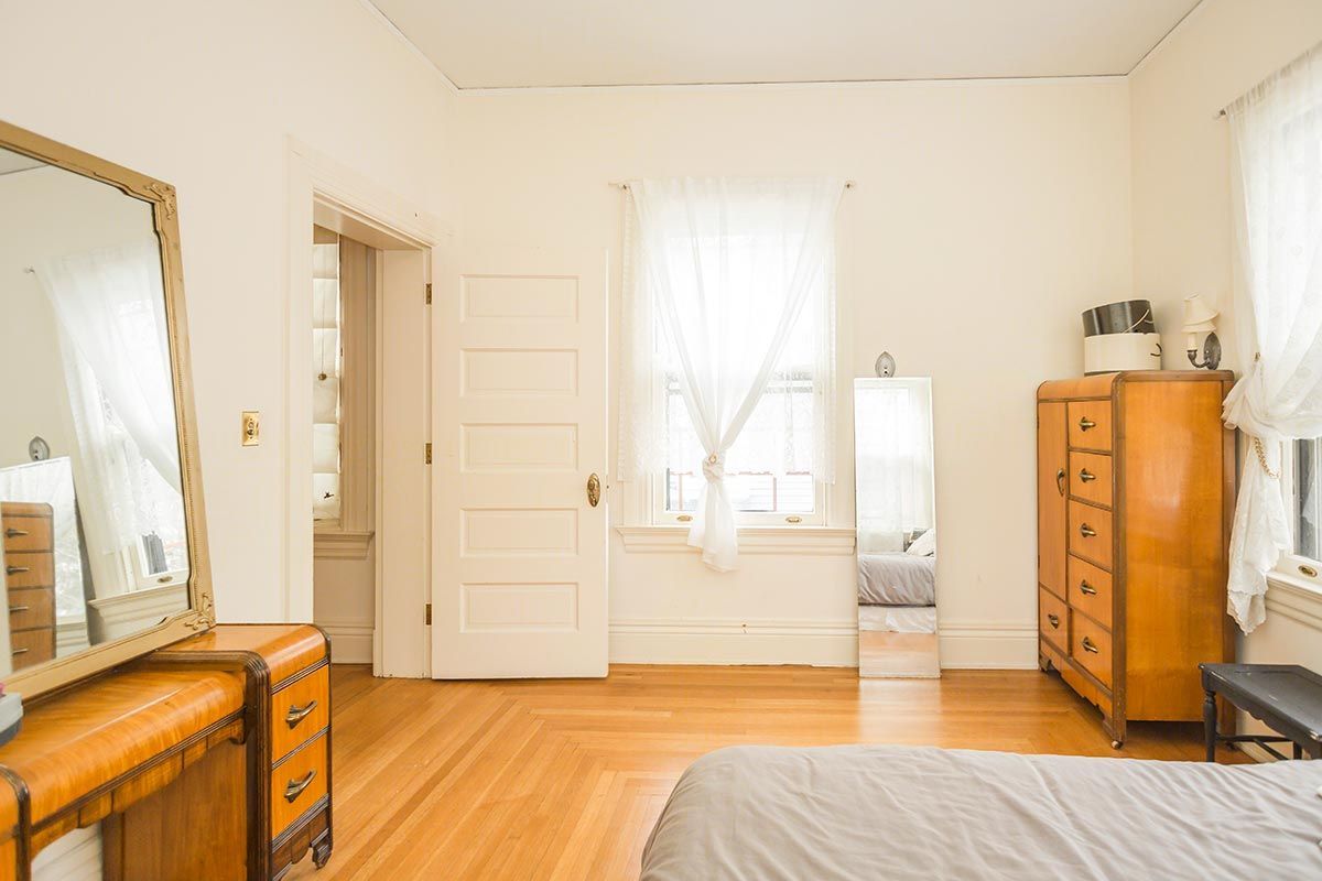 A bedroom with a bed , dresser , mirror and window.