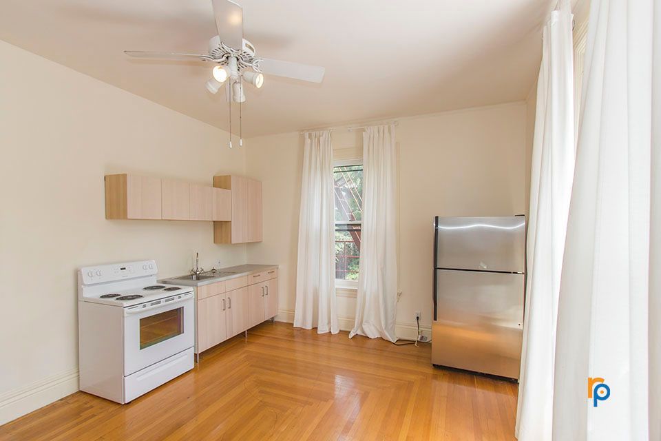 A kitchen with a stove , sink , cabinets and a ceiling fan.
