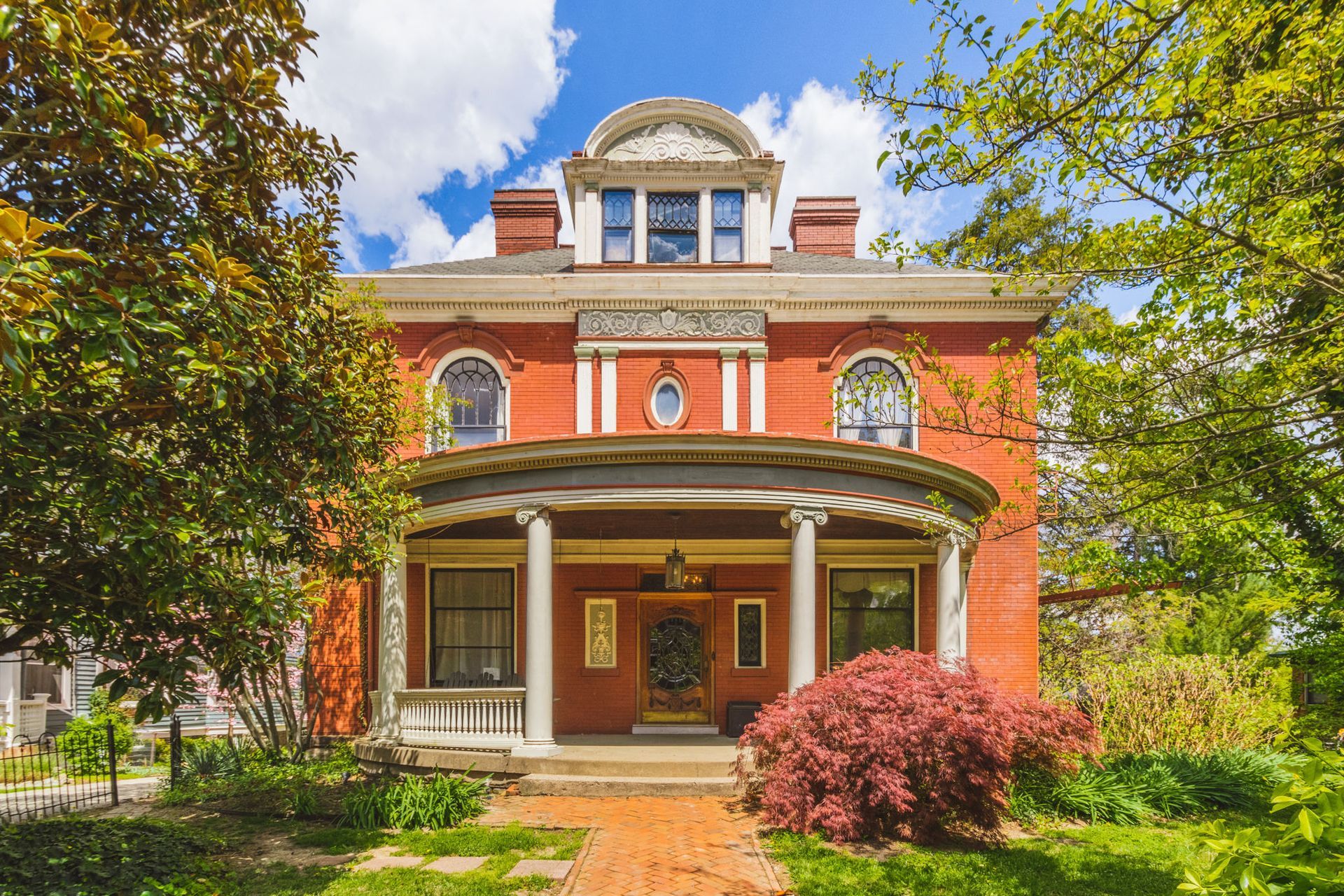 A large red brick house with a large porch and trees in front of it.