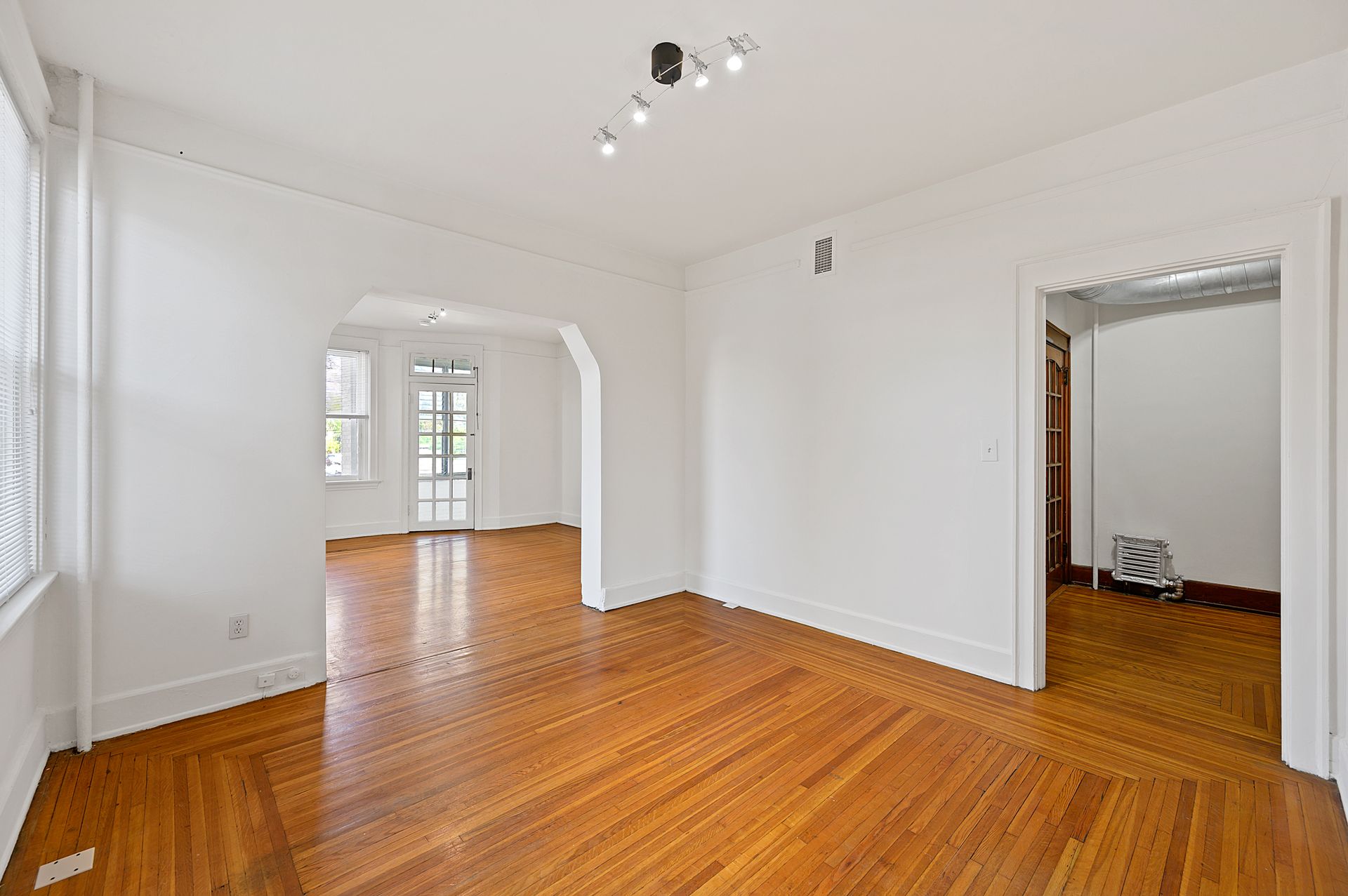 An empty living room with hardwood floors and white walls.