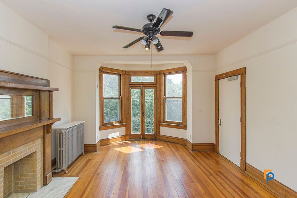 An empty living room with hardwood floors , a fireplace and a ceiling fan.