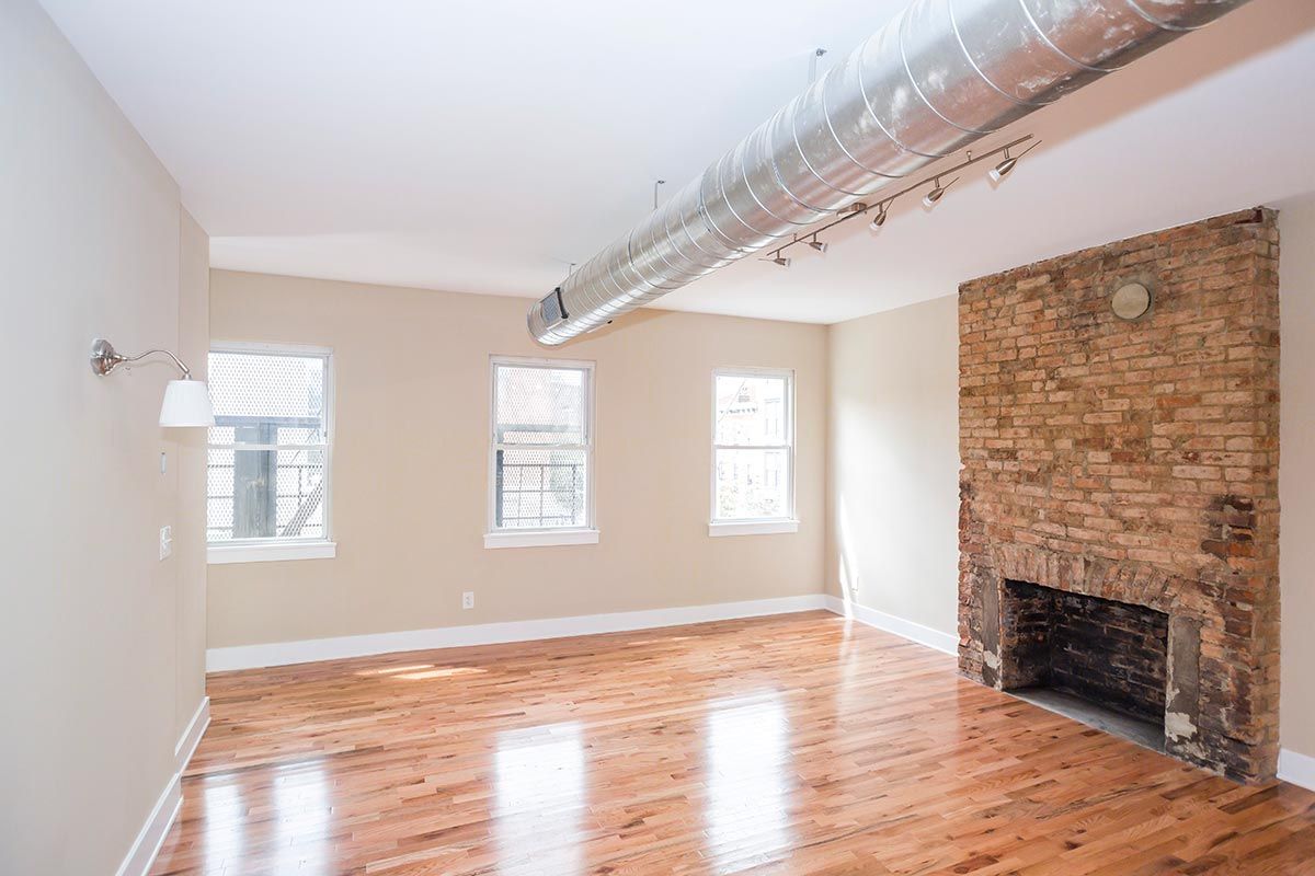 An empty living room with hardwood floors and a brick fireplace.