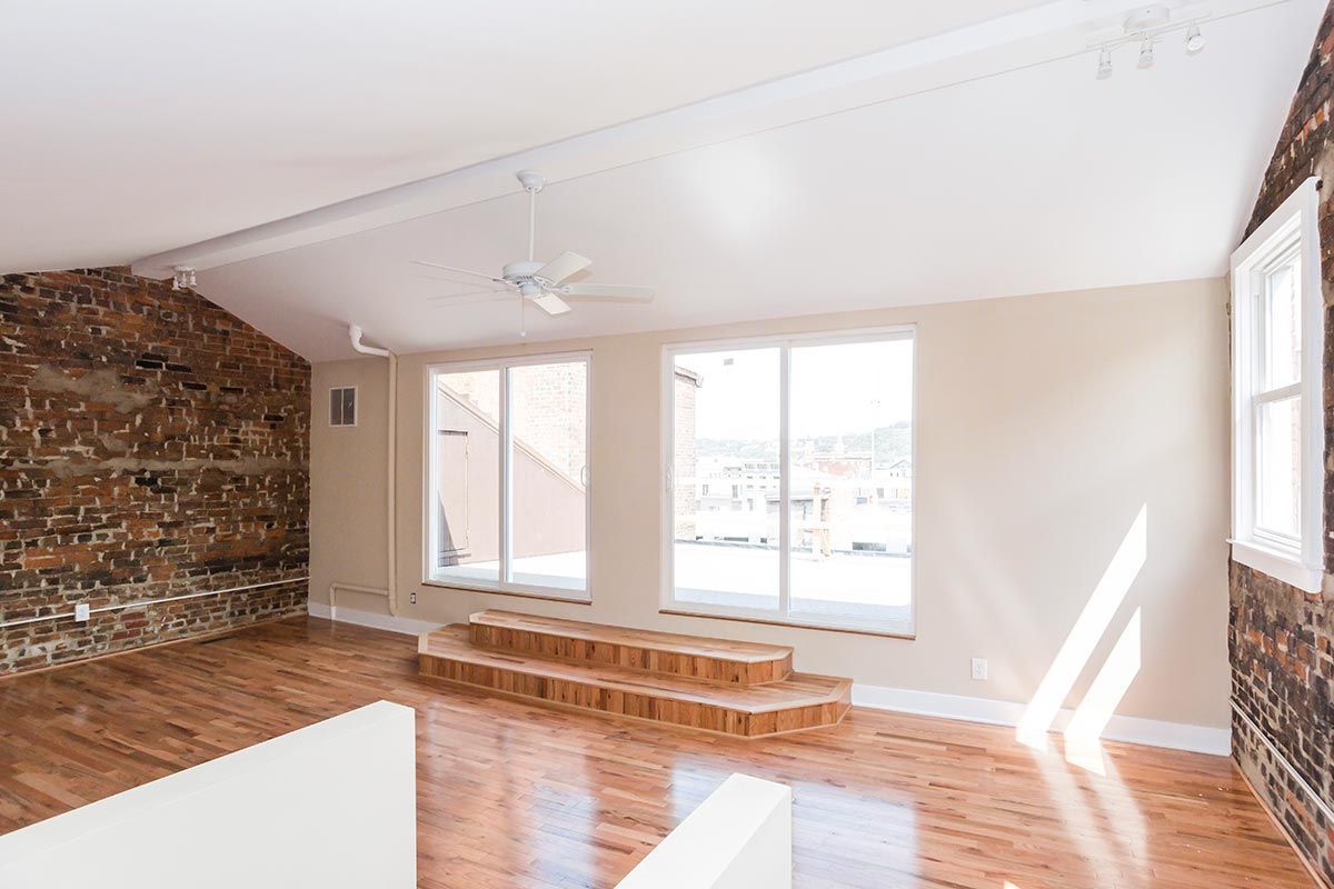 An empty living room with hardwood floors and a brick wall.