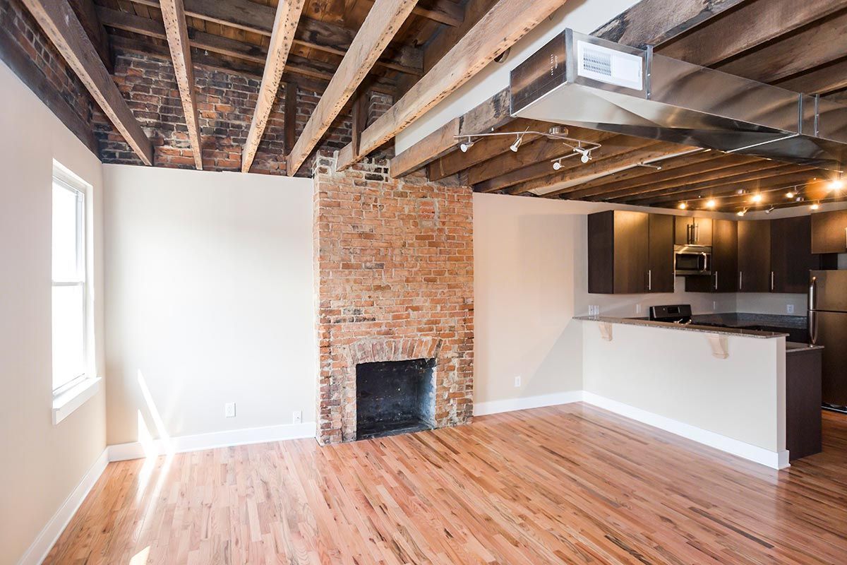 An empty living room with a fireplace and a kitchen.