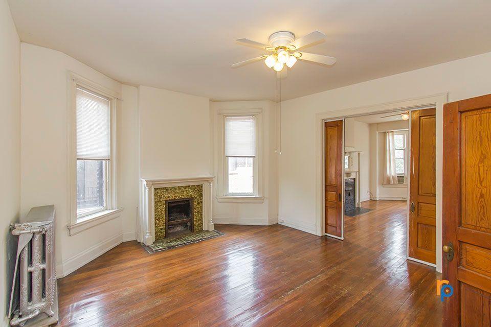 An empty living room with hardwood floors , a fireplace and a ceiling fan.