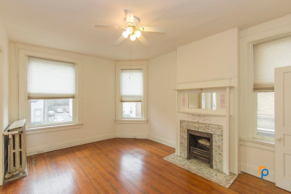 An empty living room with a fireplace and a ceiling fan.