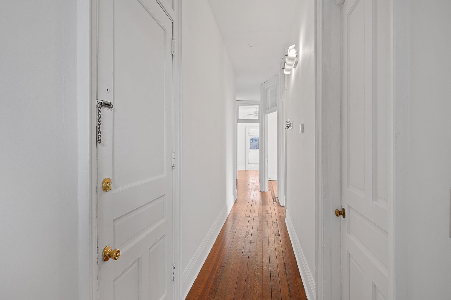 A long hallway with white walls and wooden floors in a house.