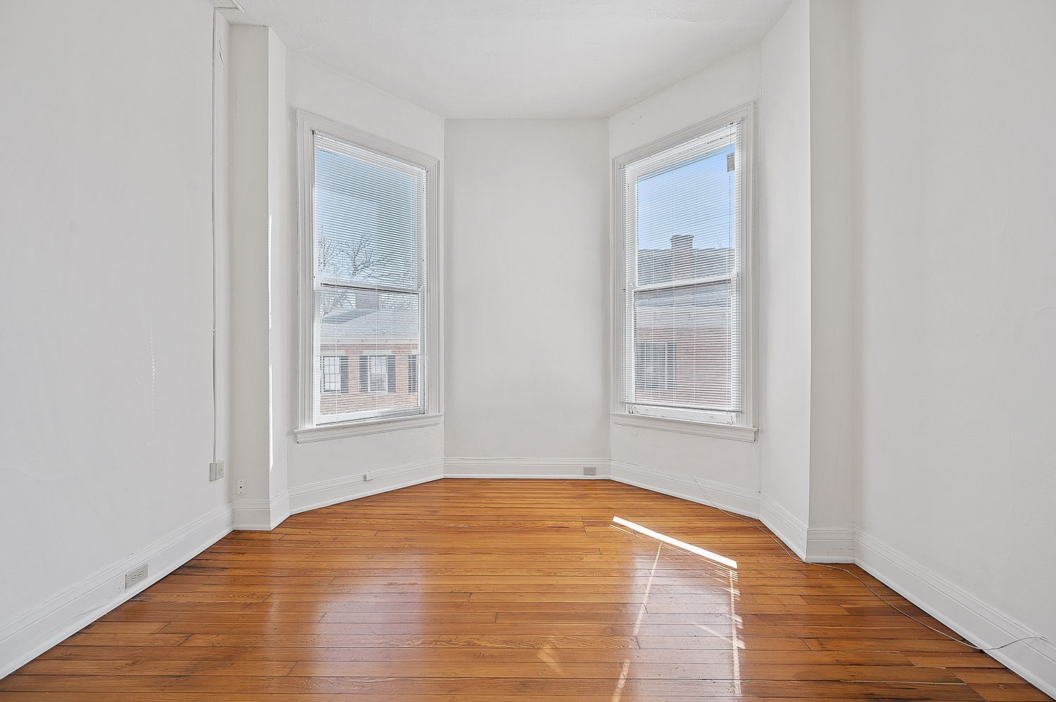 An empty room with hardwood floors and two windows.