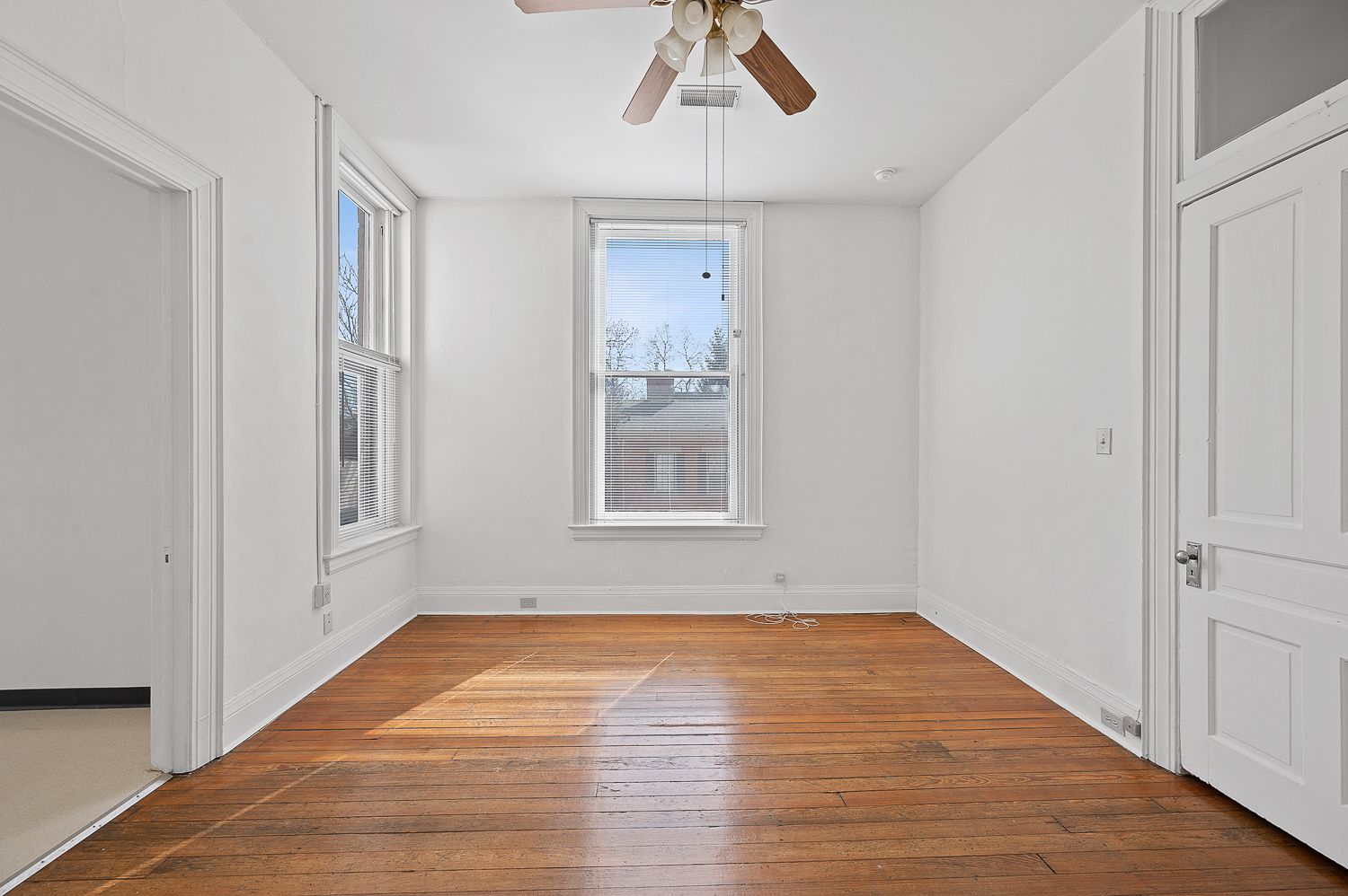 An empty room with hardwood floors and a ceiling fan.