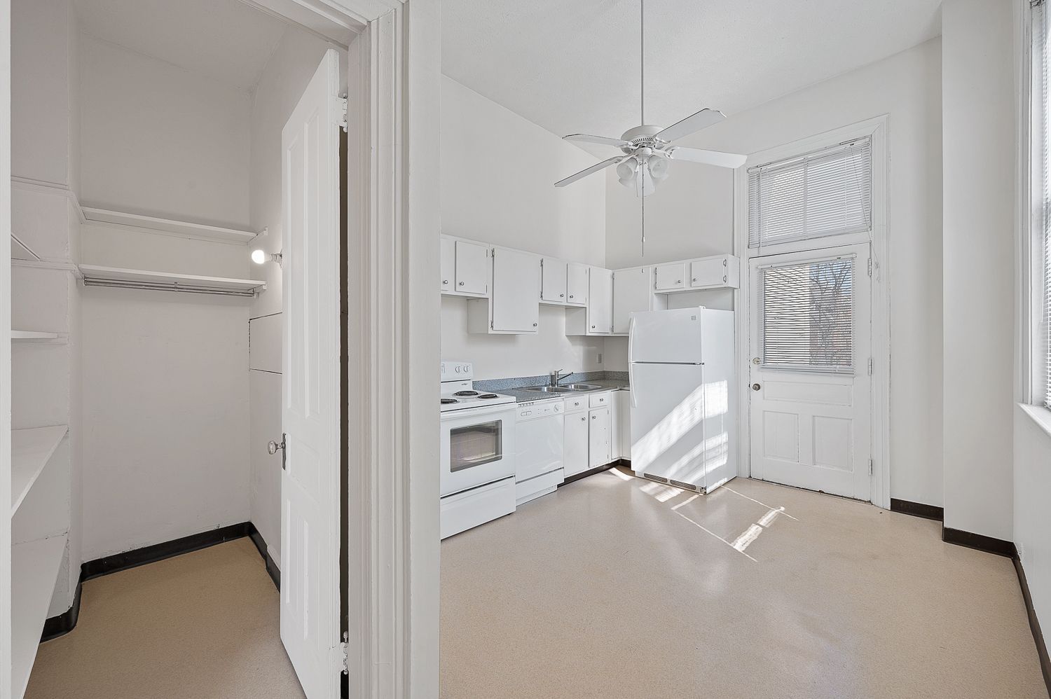 A kitchen with white cabinets , a refrigerator , a stove , and a ceiling fan.