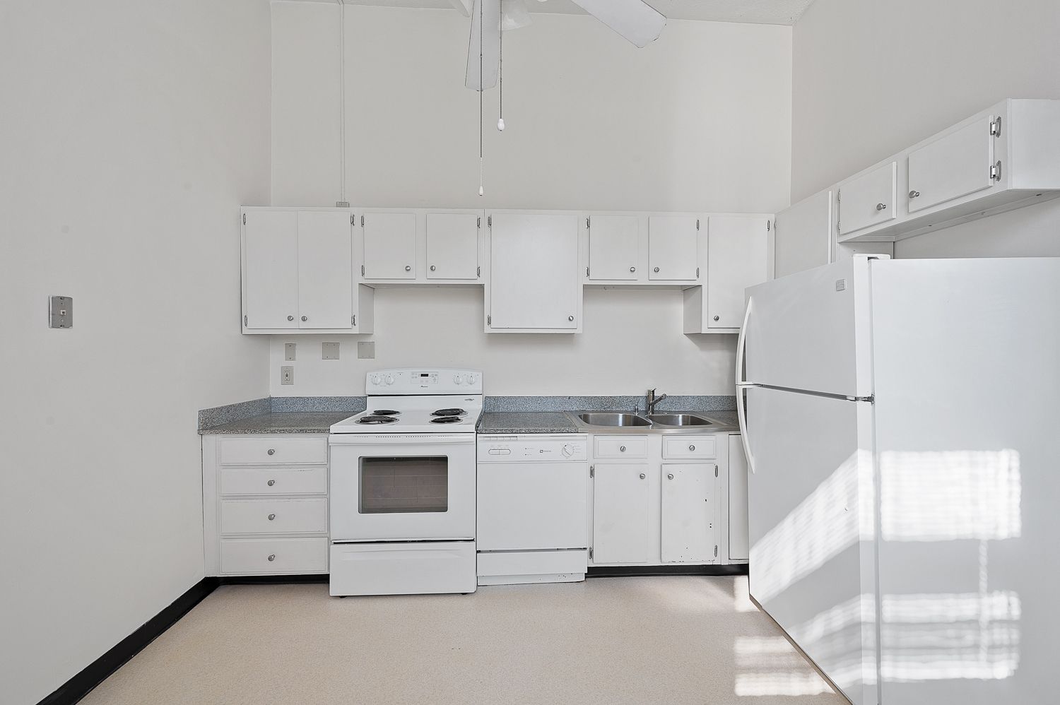An empty kitchen with white cabinets and appliances