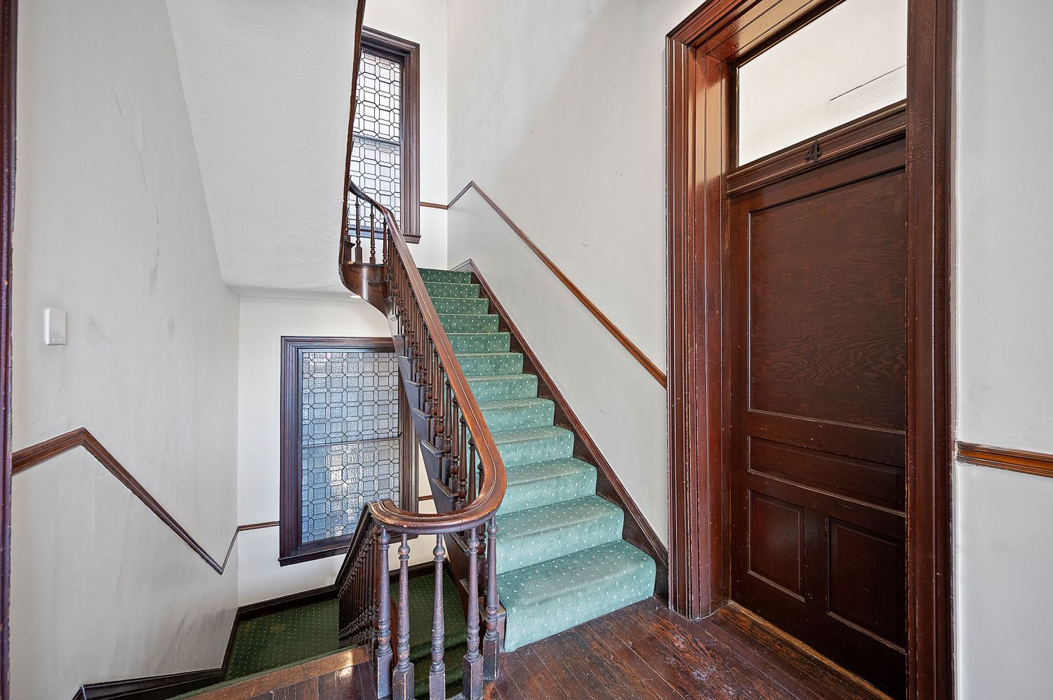 A staircase with green carpet and a wooden railing