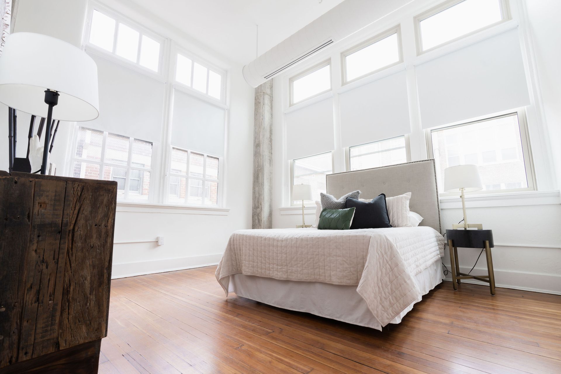 A bedroom with a bed , nightstand , and lots of windows.