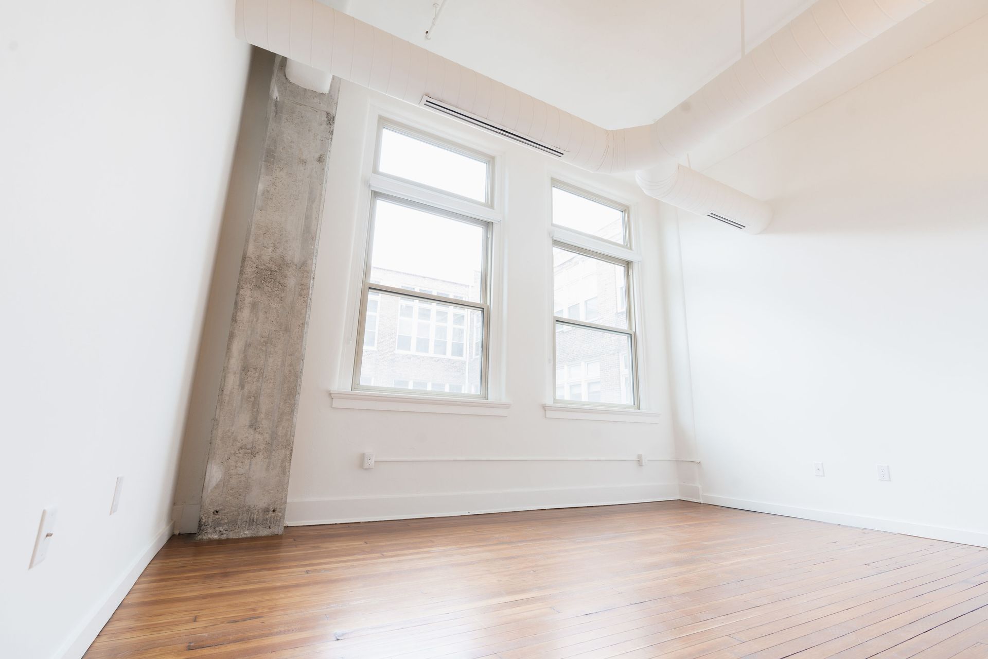 An empty room with hardwood floors and two windows.