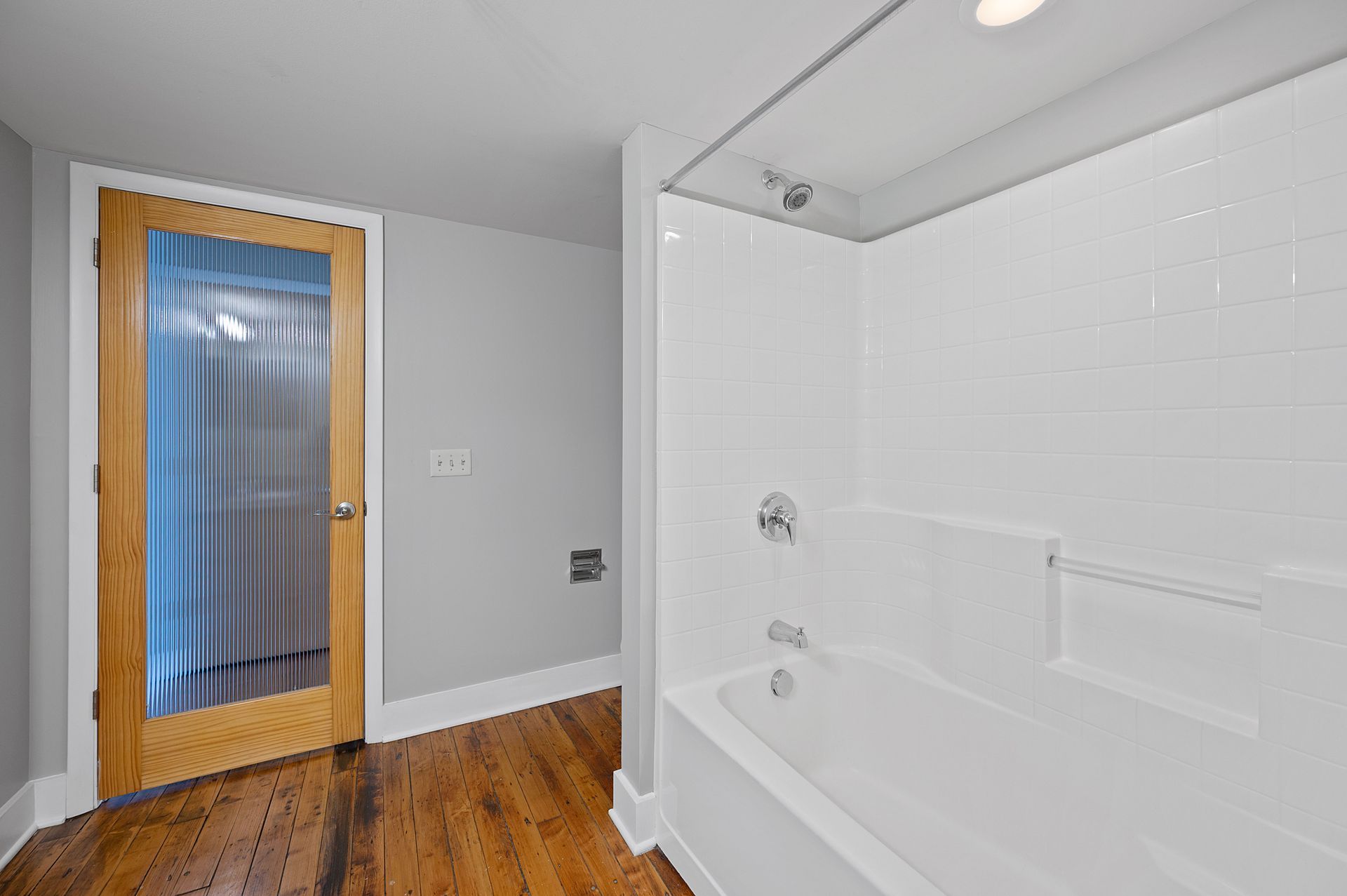 A bathroom with a bathtub , shower , and wooden floor.