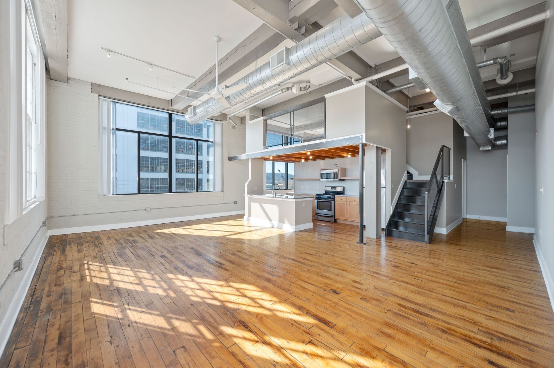 A large empty room with hardwood floors and a staircase leading to the second floor.