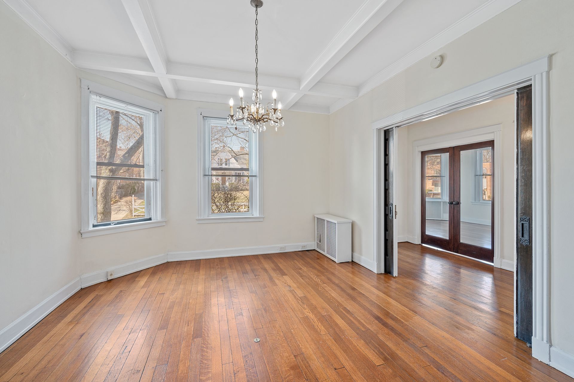 An empty living room with hardwood floors and a chandelier hanging from the ceiling.
