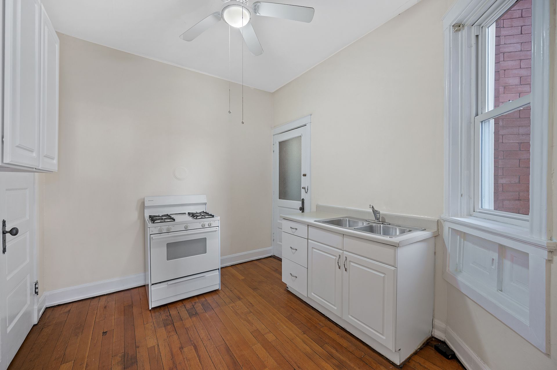An empty kitchen with a stove , sink , and ceiling fan.