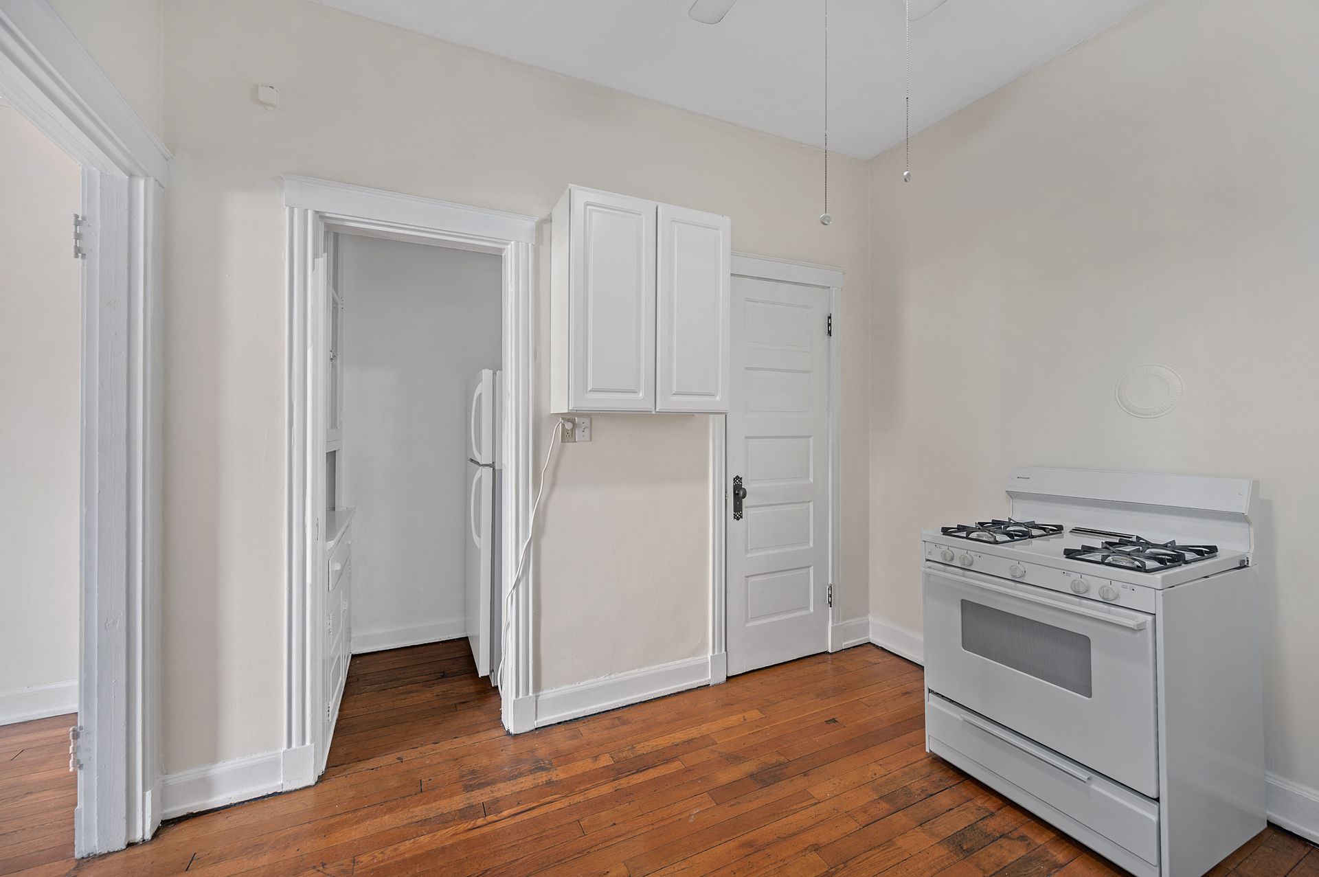 An empty kitchen with a white stove and a refrigerator.
