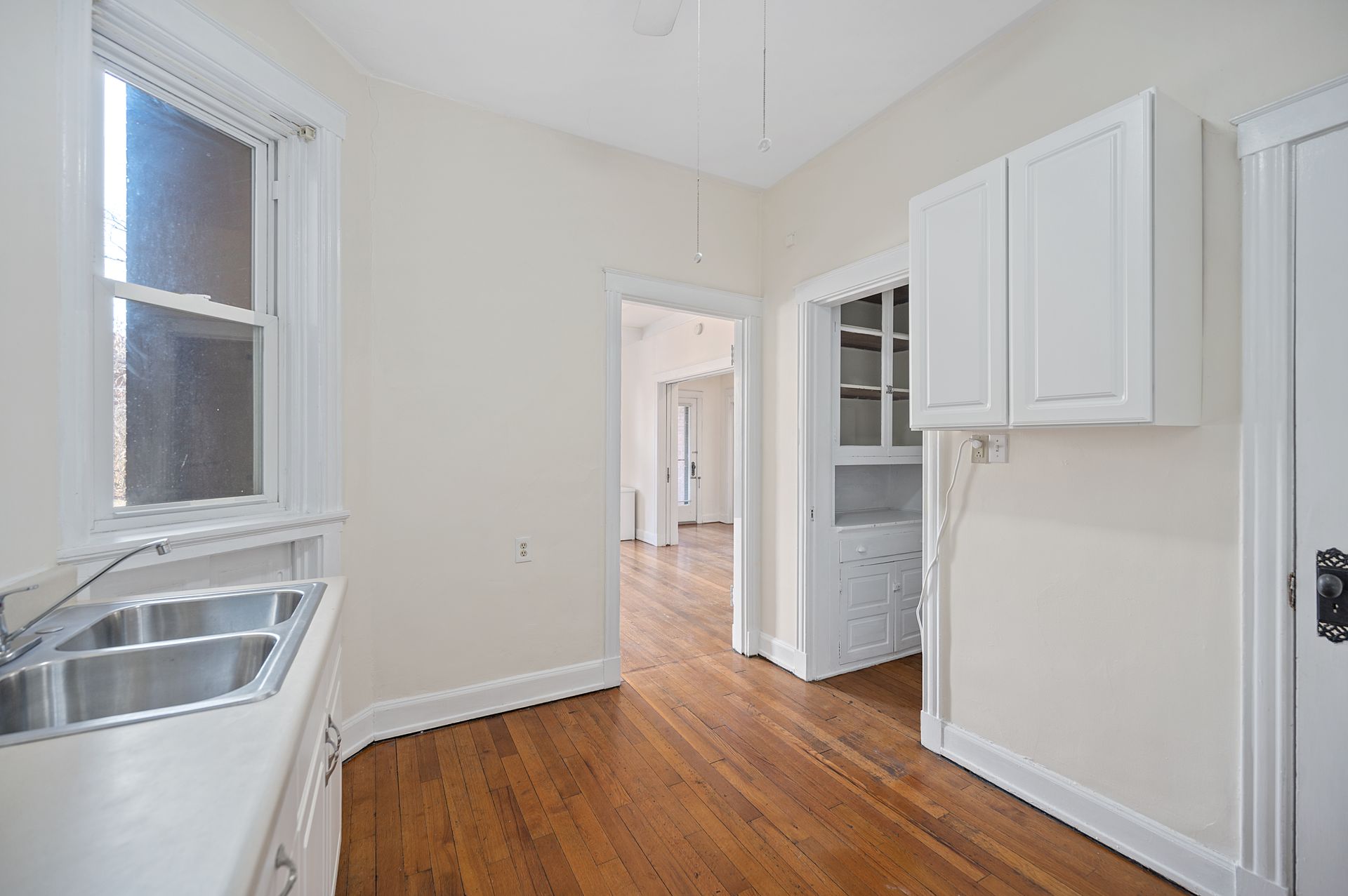An empty kitchen with white cabinets and hardwood floors
