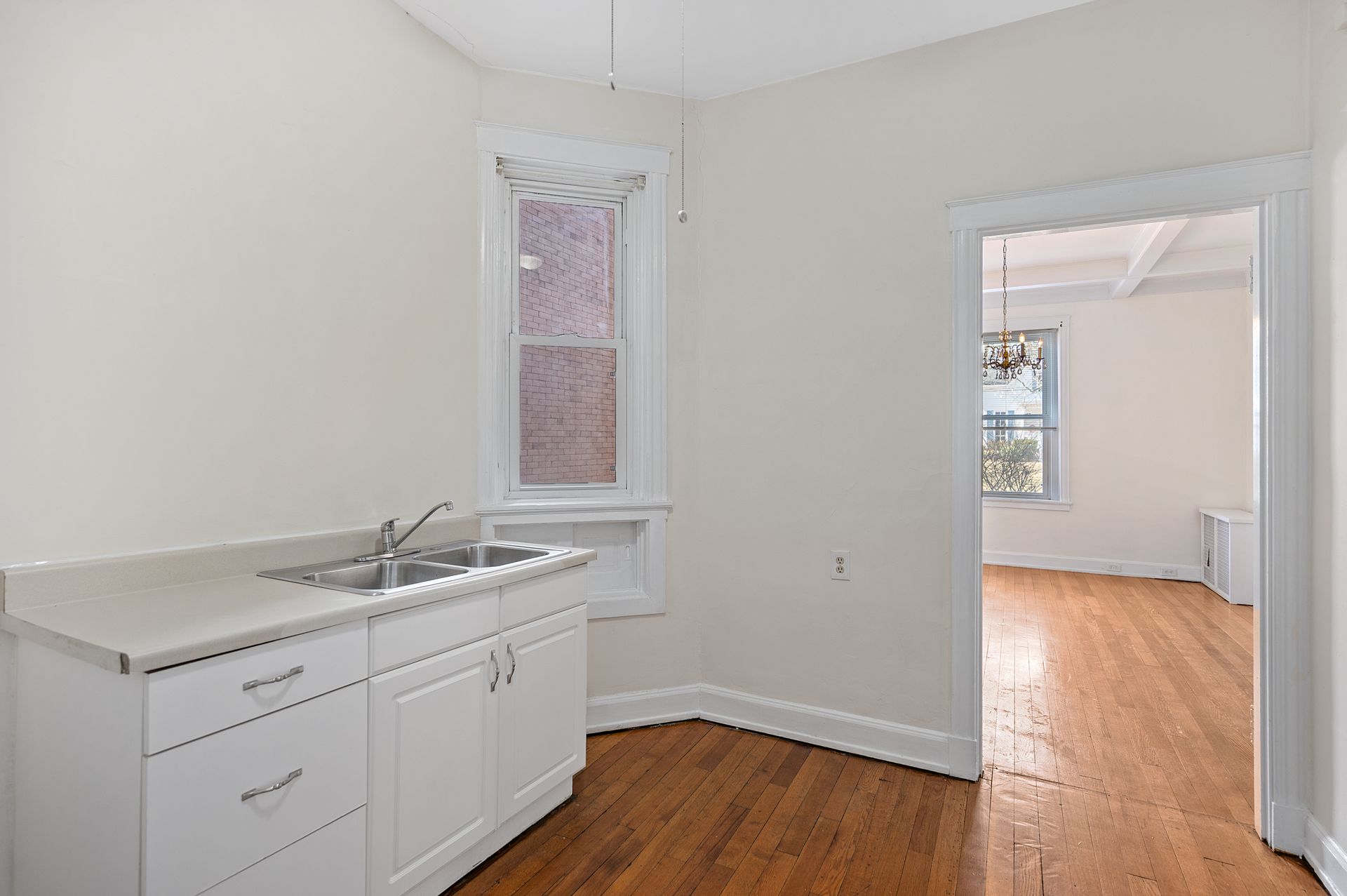 An empty kitchen with a sink , cabinets and hardwood floors.