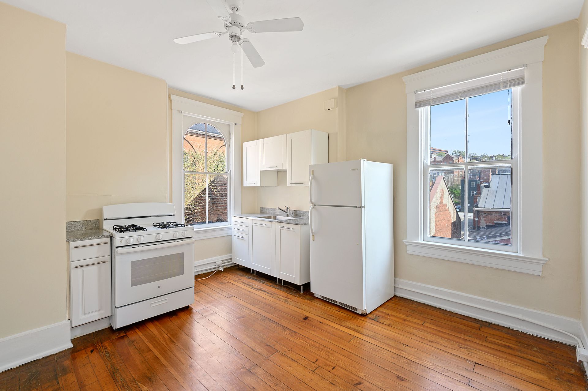 An empty kitchen with a stove , refrigerator , cabinets and a ceiling fan.