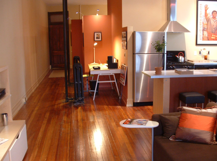 A living room with hardwood floors and a stainless steel refrigerator