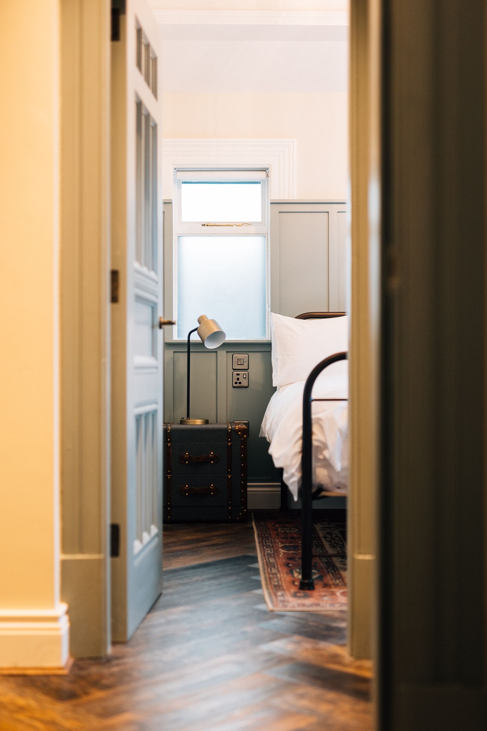 Bedroom interior framed by an open door. A bed with a black frame and white bedding is visible