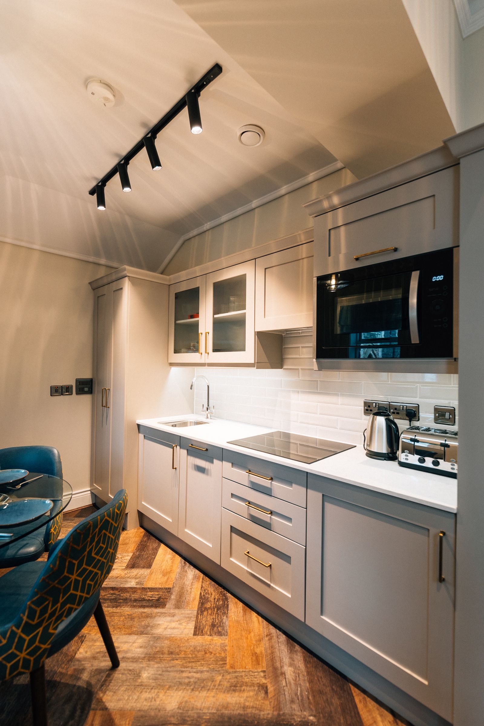 A small, modern kitchen with light gray cabinets, white countertops, and a microwave.