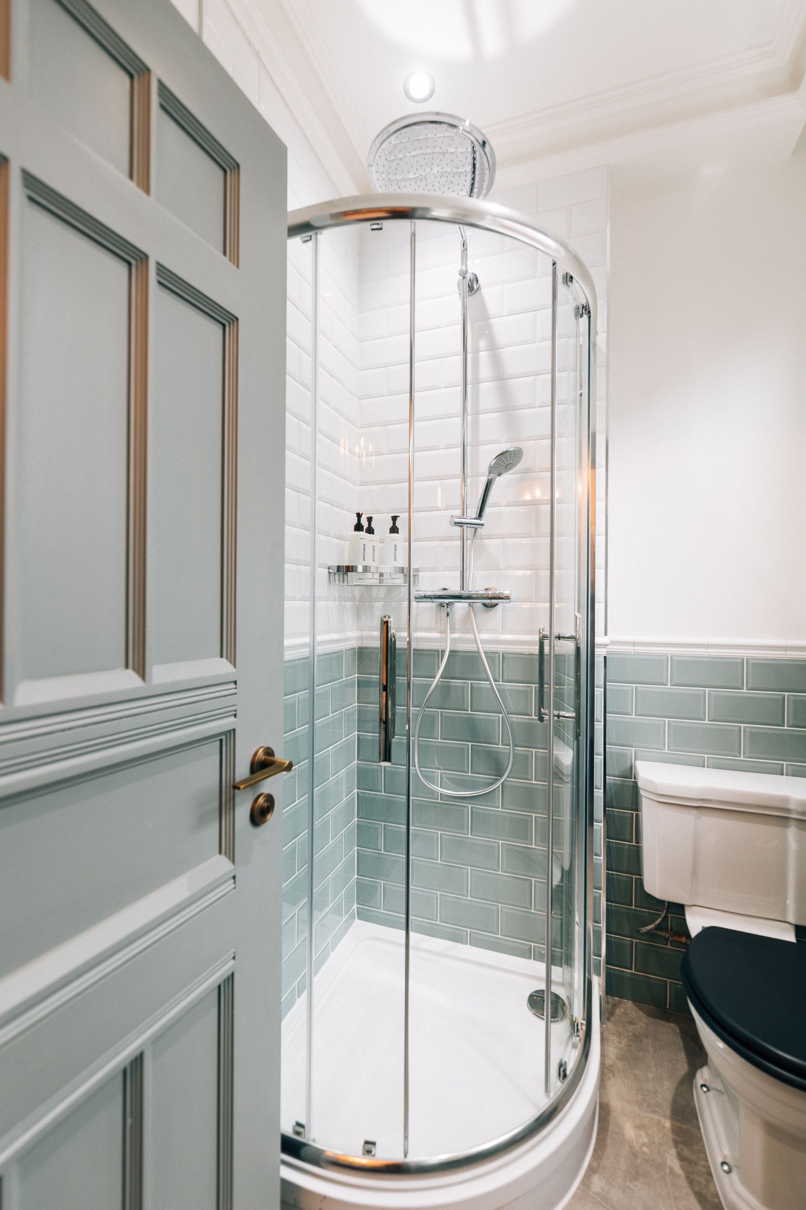 Bathroom with a glass corner shower, mint tile walls, and a toilet beside an open door.