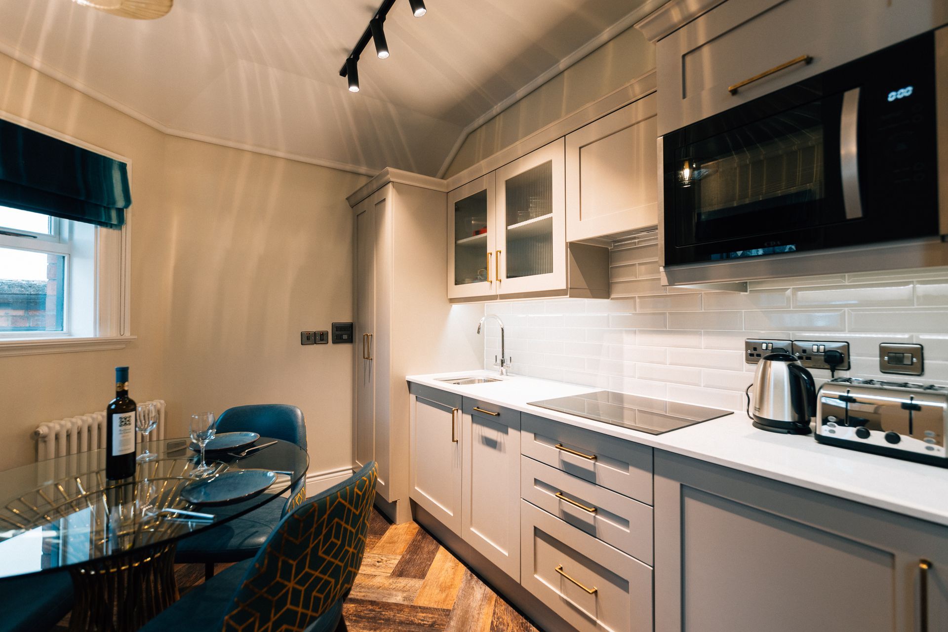 A small kitchen and dining area with light gray cabinets, a black microwave, a glass dining table, and blue chairs.