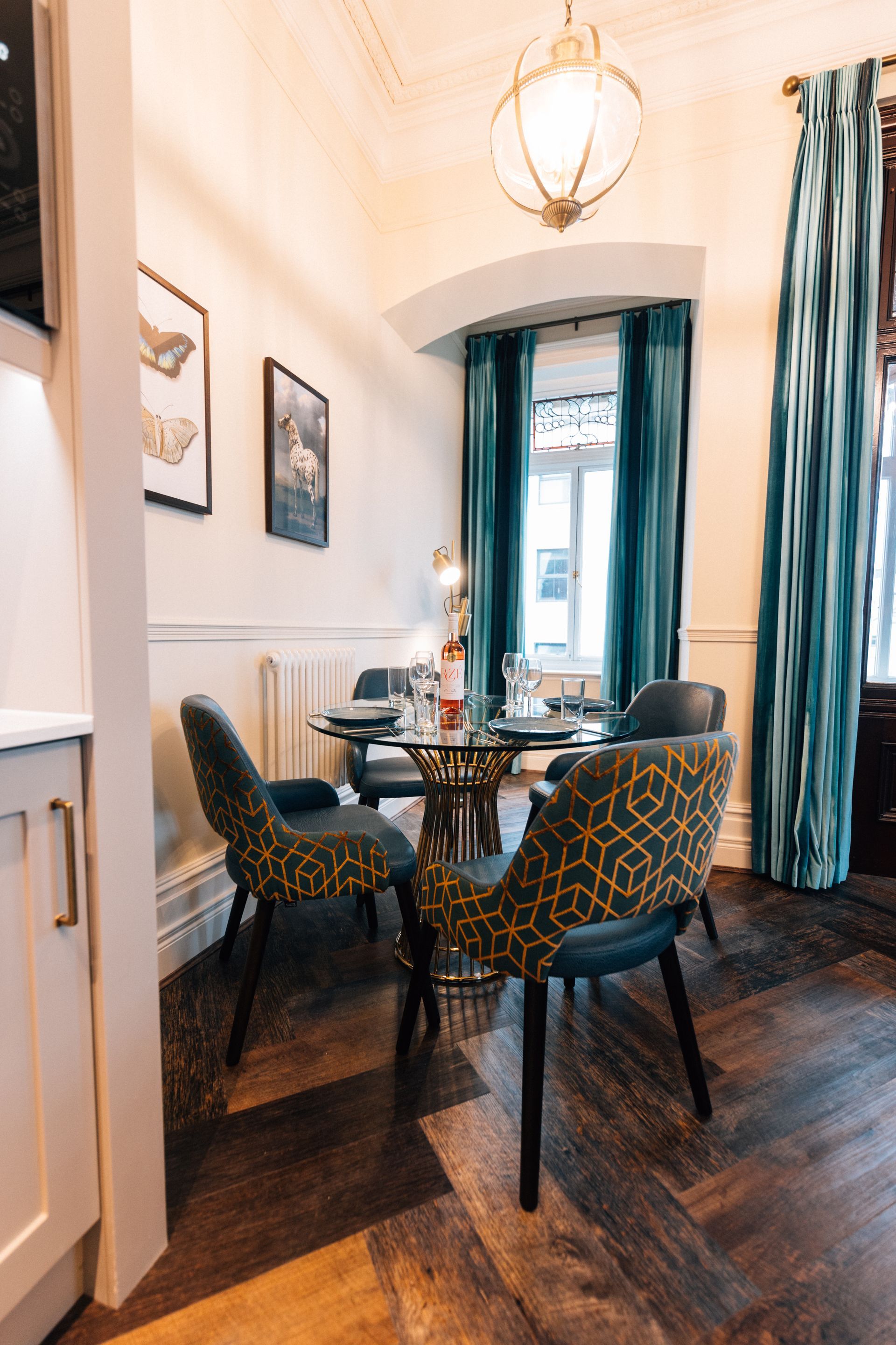 Dining room with a round table, patterned chairs, teal curtains, and a decorative light fixture.